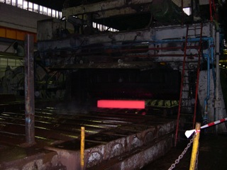 Bild: Das Breite Umkehr Walzwerk. Walzen von Kupfer-Nickel-Blechen. Das glühende Vormaterial passiert das Walzgerüst.