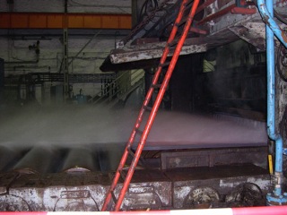 Bild: Das Breite Umkehr-Walzwerk. Walzen von Kupfer-Nickel-Blechen. Das Blech wird mit Hilfe von Druckwasser vom Zunder befreit.